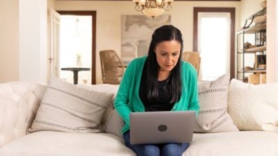 Lady sitting on her couch typing on a laptop at home